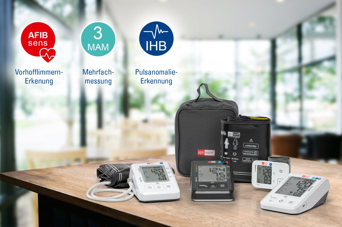 Aponorm Blutdruckmessgeräte: vier verschiedene Modelle mit Tasche liegen auf einem holzernen Tisch. Der Hintergrund ist verschwommen.