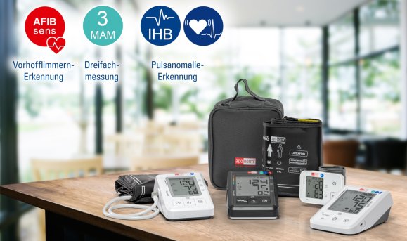 BMG Web Technologien Aponorm Blutdruckmessgeräte: vier verschiedene Modelle mit Tasche liegen auf einem holzernen Tisch. Der Hintergrund ist verschwommen.