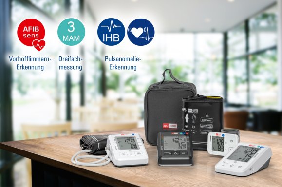 BMG Web Technologien Aponorm Blutdruckmessgeräte: vier verschiedene Modelle mit Tasche liegen auf einem holzernen Tisch. Der Hintergrund ist verschwommen.